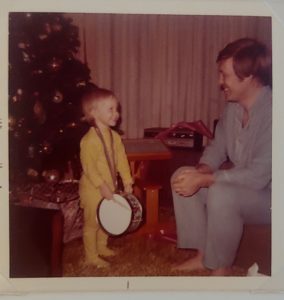 Man smiling at his young daughter by a Christmas tree. 