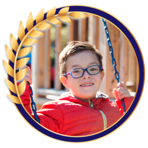 A boy with Down syndrome on a swing. There is gold laurels around the frame.